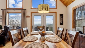 A dining area with a wooden table, six chairs, a central wooden bowl, and a hanging light fixture. - Private Mountain Cabin Retreat 1.5 acres, Amazing Views, Hot Tub, STARLINK Wifi (Murphy)