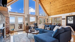 A spacious living room with a large blue sectional sofa, a fireplace, and large windows offering views of the outdoors. - Private Mountain Cabin Retreat 1.5 acres, Amazing Views, Hot Tub, STARLINK Wifi (Murphy)