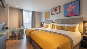Een hotelkamer met een groot bed, twee nachtkastjes, een klein bureau met een stoel, en een raam met gordijnen.