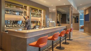 Een moderne bar met een bartender, drankenkasten en oranje barkrukken.