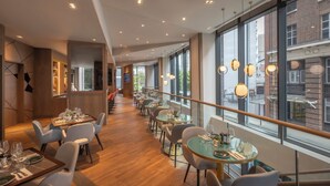 Een modern restaurant met een lange eetruimte, houten vloeren en grote ramen met uitzicht over de stad.