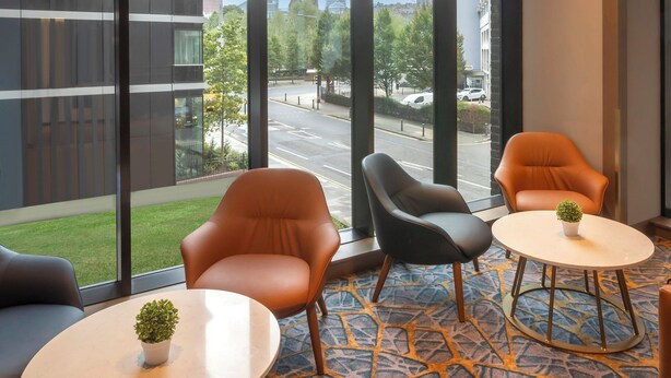 Een hotelkamer met grote ramen, twee stoelen, een bijzettafeltje en een potplant.
