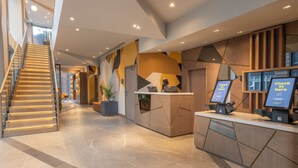 Een moderne hotellobby met een receptiebalie, een trap en een geometrisch wandontwerp.