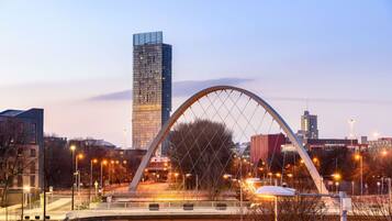 A modern bridge with a distinctive arch design, connecting two parts of a cityscape with high-rise buildings in the background.
