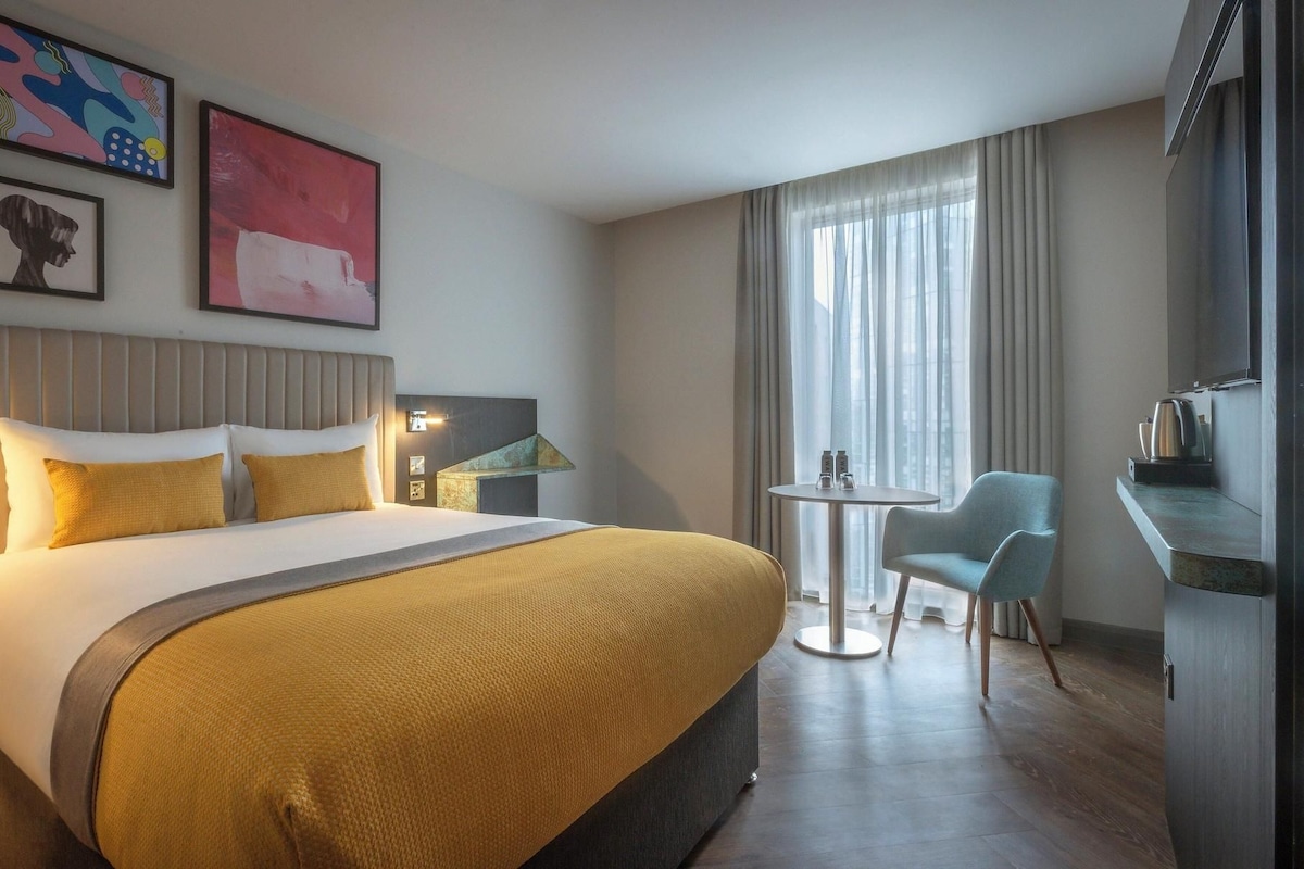 Ein Hotelzimmer mit einem großen Bett, einem kleinen runden Tisch, einem Stuhl und einem Fernseher.