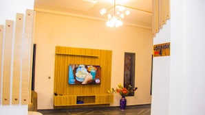 Un vestíbulo con un televisor fijado a un panel de madera, un jarrón con flores y un cartel que indica el área de descanso.