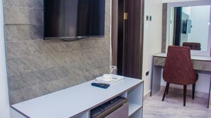Un baño moderno con un espejo grande, un tocador con lavabo y un televisor montado en la pared.