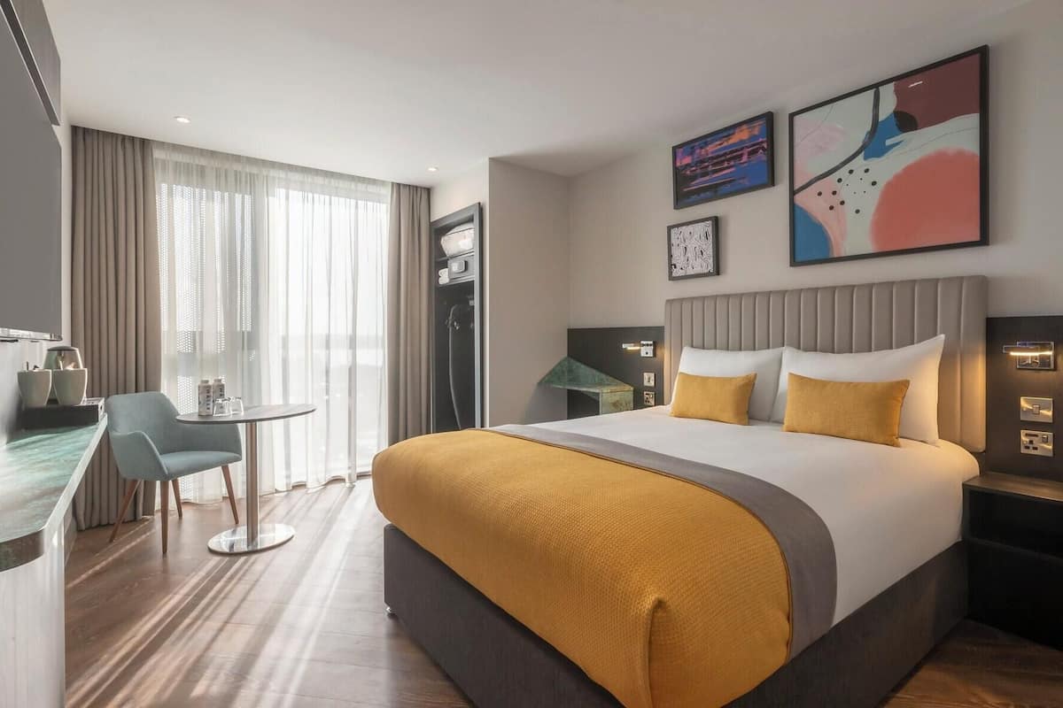 A hotel room with a bed, a desk, a chair, and a TV.