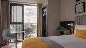 A hotel room with a bed, a table, a chair, a TV, and a view of a Ferris wheel.