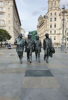 A statue of four figures walking on a paved area with buildings in the background.