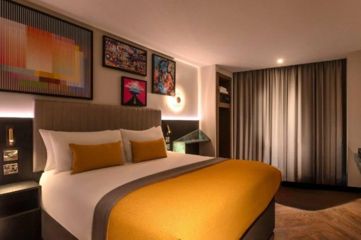 A hotel room with a large bed, a nightstand, a desk, and a window with curtains.
