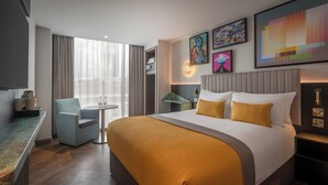 A hotel room with a large bed, a desk with a chair, a small round table with two cups and a kettle, and a window with curtains. - Maldron Hotel Shoreditch London (London)