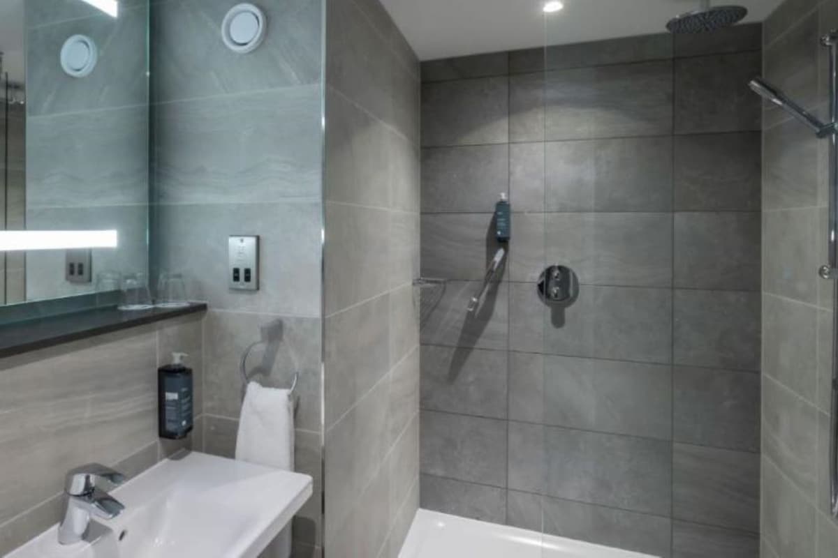Une salle de bain moderne avec une douche à l’italienne en verre, un lavabo blanc et un grand miroir.