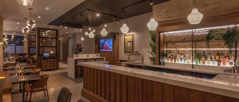 A modern bar area with a wooden counter, seating, and hanging pendant lights.