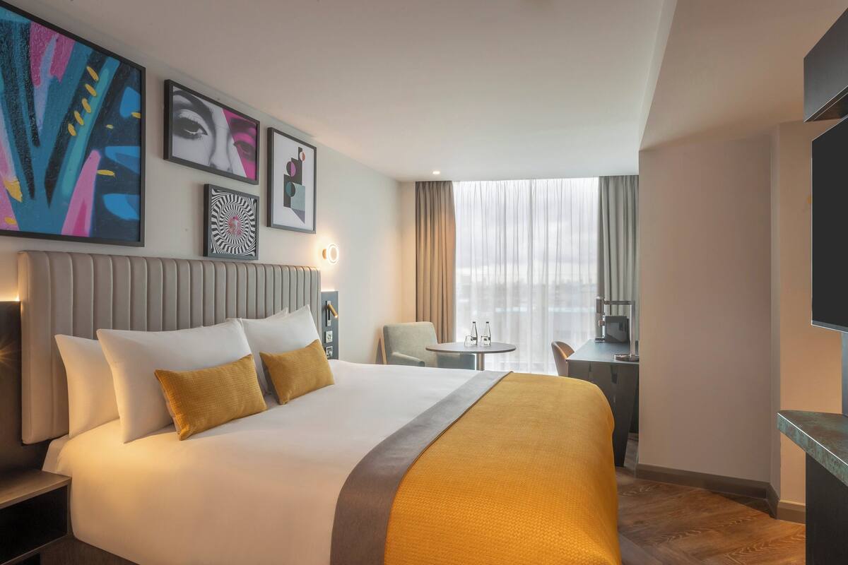 A hotel room with a large bed, a desk, a chair, and a TV.