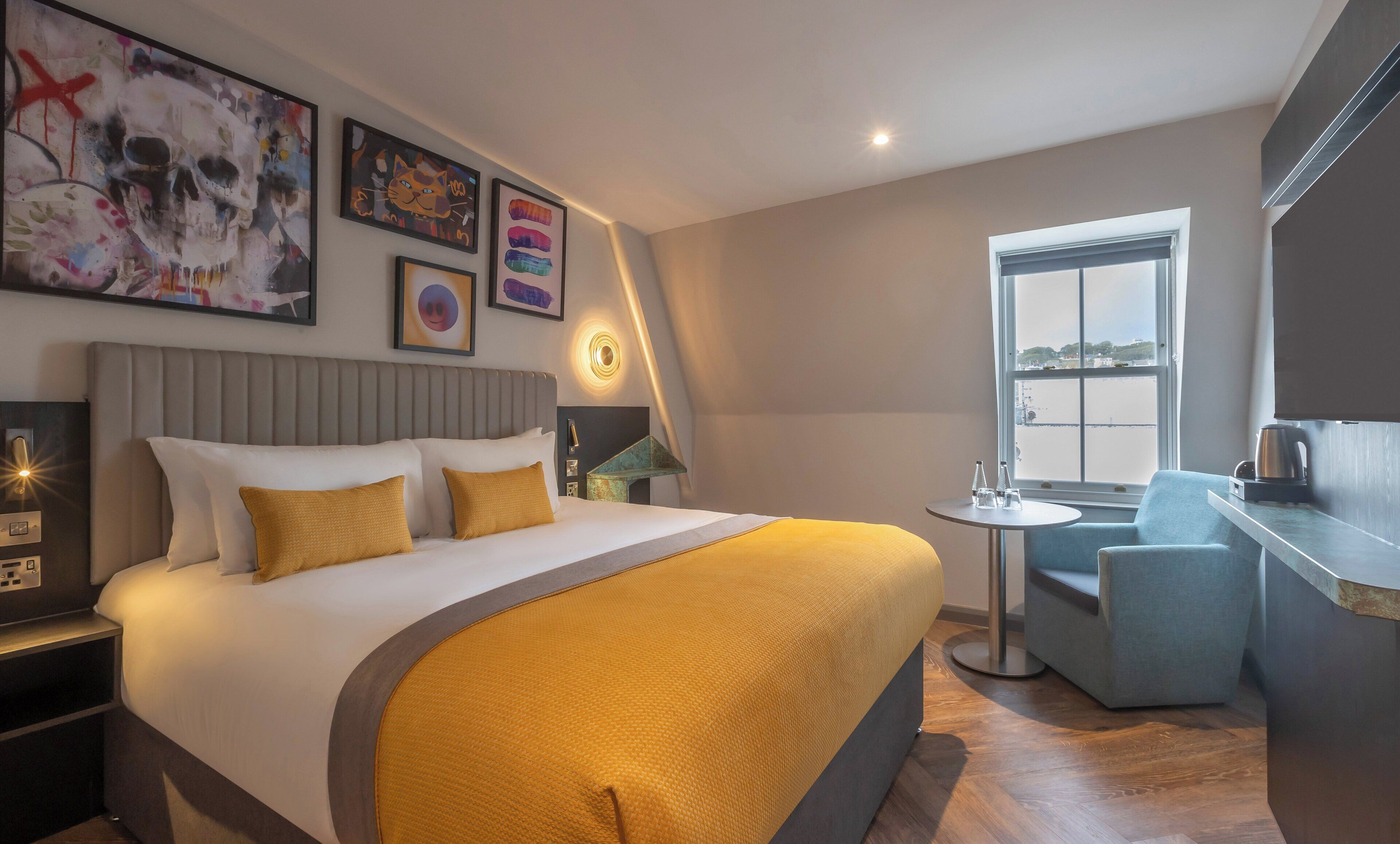 A modern hotel room with a large bed, a small round table, a seating area, and artwork on the walls.