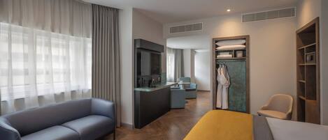 A modern hotel room with a sofa, a bed, a TV, a desk, and a bathroom with a robe and towel rack.