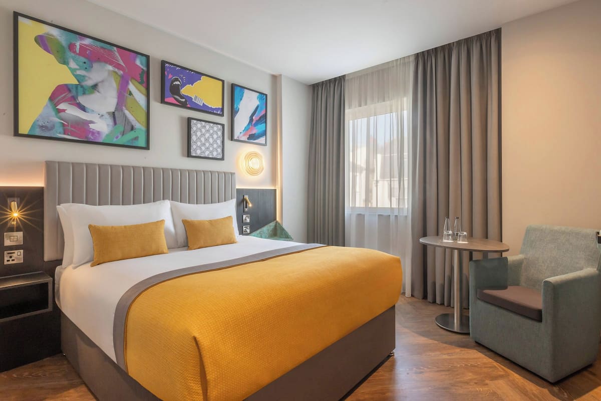 A hotel room with a large bed, a small round table, a chair, and artwork on the walls.