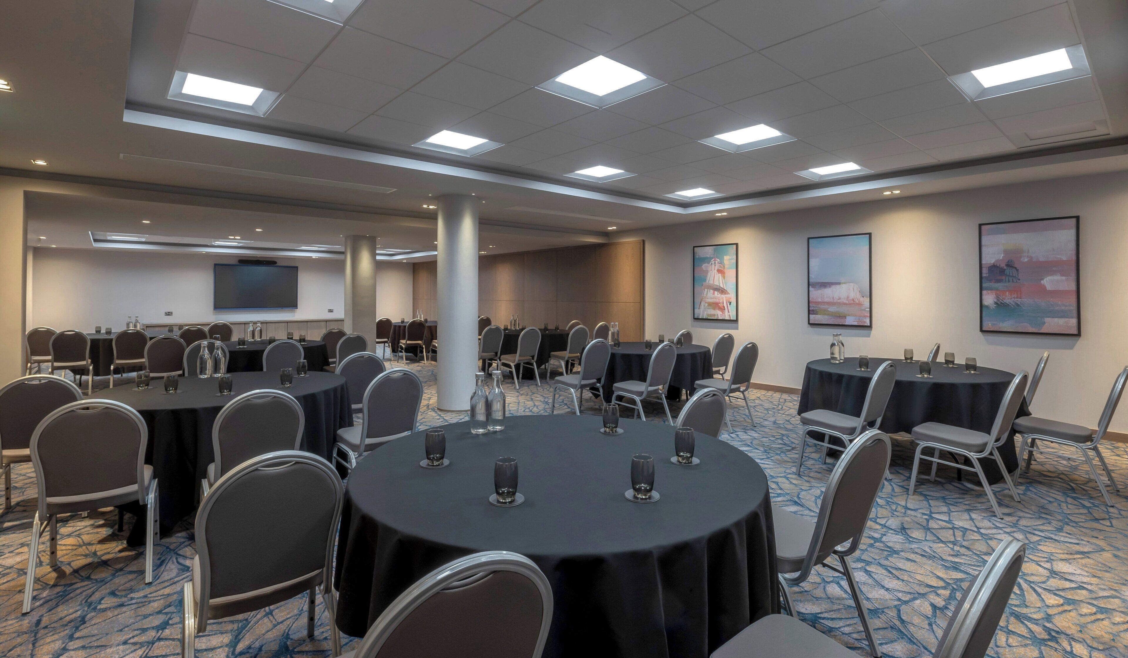Une salle de conférence équipée de tables rondes, de chaises, d’un grand écran et d’œuvres d’art accrochées aux murs.