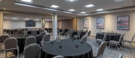 Une salle de conférence équipée de tables rondes, de chaises, d’un grand écran et d’œuvres d’art accrochées aux murs.