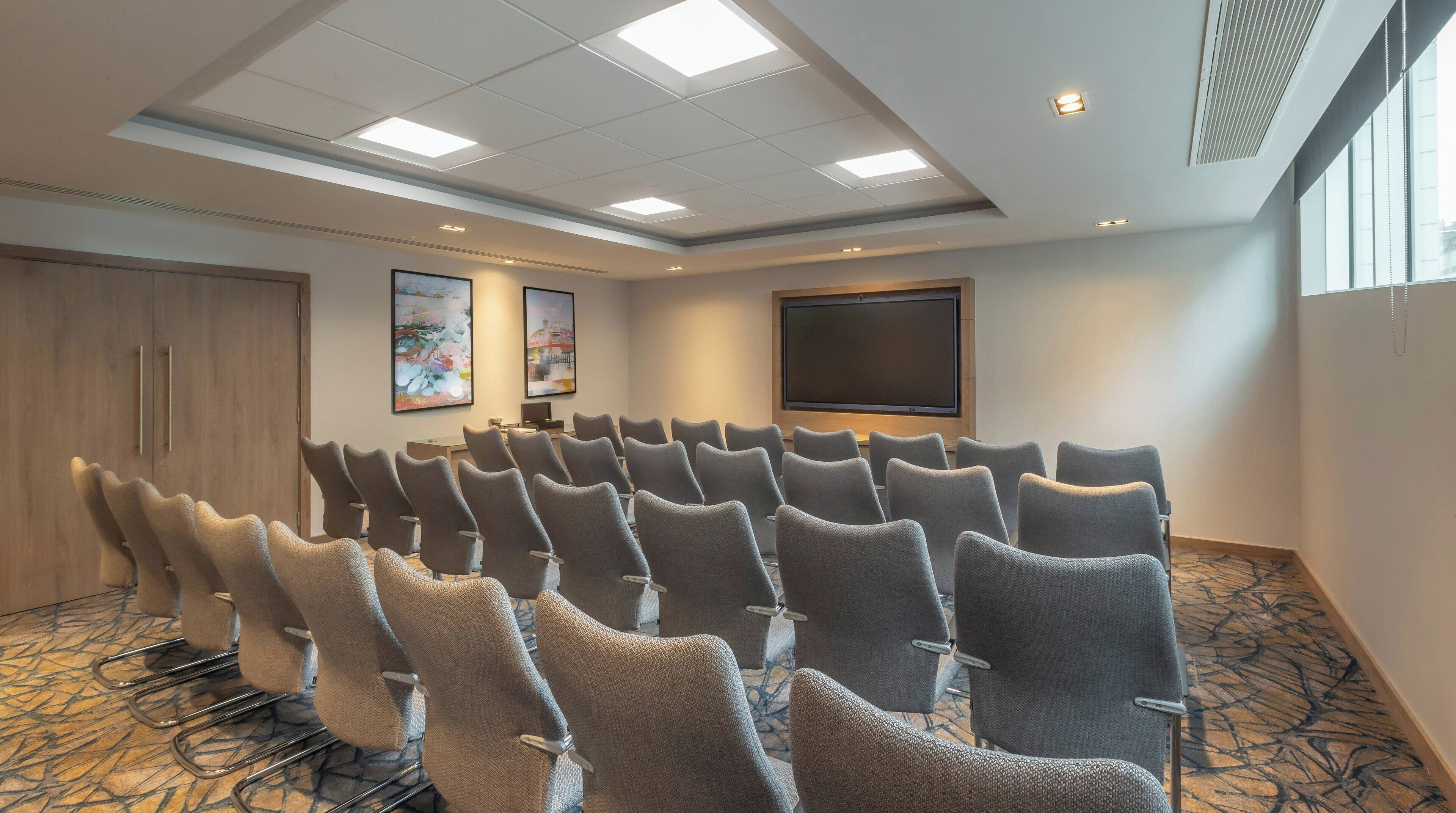 A conference room with rows of chairs, a large screen, and artwork on the walls.