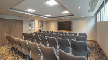 A conference room with rows of chairs, a large screen, and artwork on the walls.