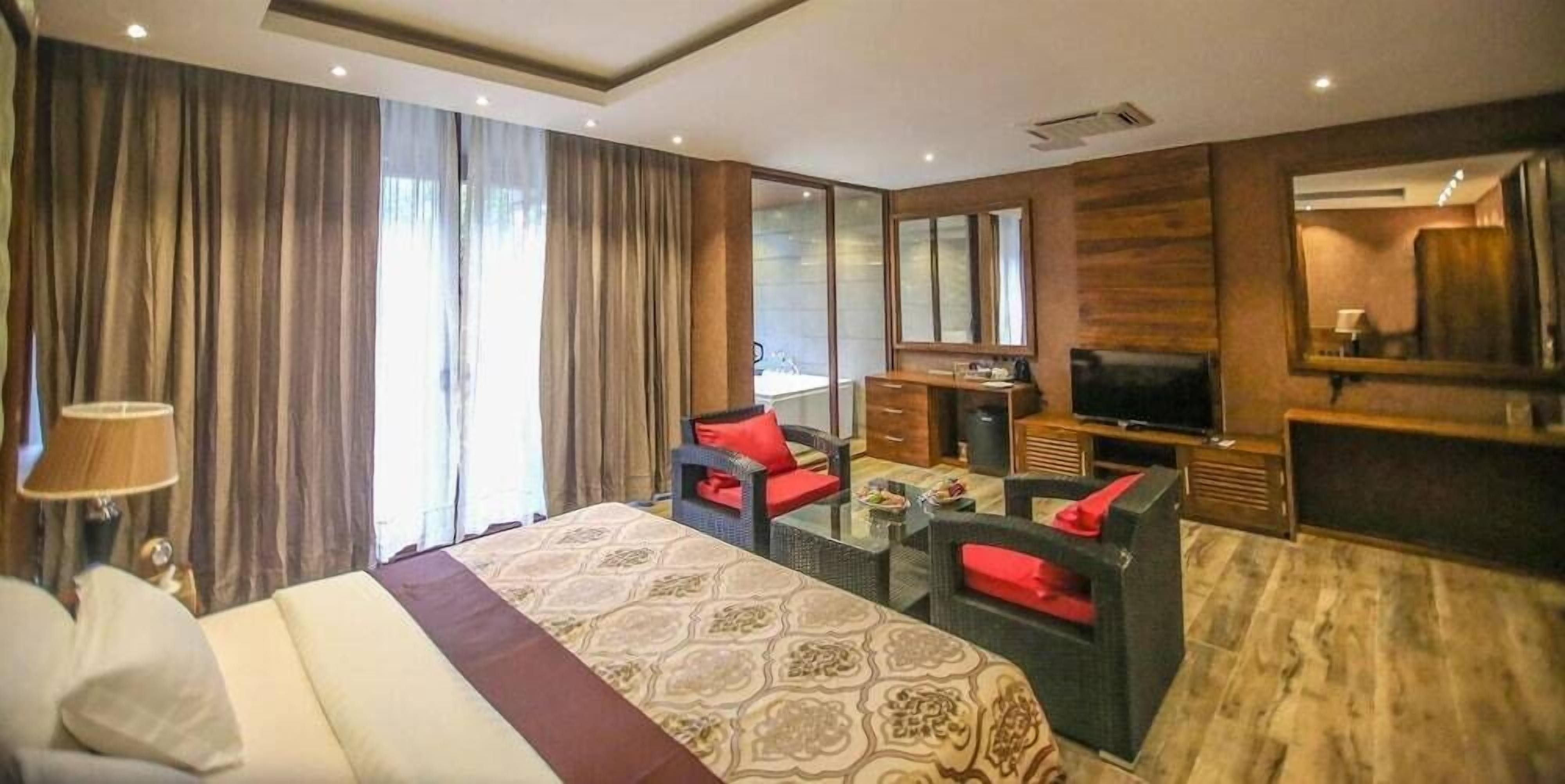 A hotel room with a large bed, a TV, a desk, and a seating area with red cushions.