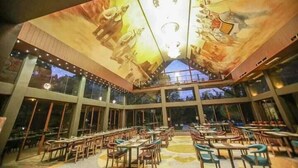 A spacious dining area with high ceilings and large windows, featuring a mural of a historical scene.
