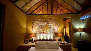A hotel room with a bed, two bedside tables, a decorative wall piece, and a ceiling with a wooden design.