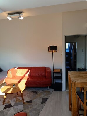 A modern living room with a red sofa, a wooden coffee table, a floor lamp, and a dining area with a wooden table and chairs.
