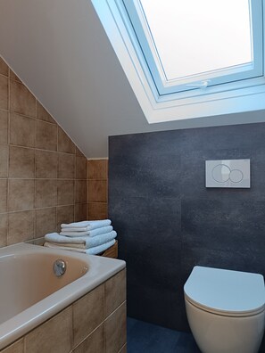 A modern bathroom with a skylight, a bathtub, a toilet, and a stack of towels. - Super apartment #4 in the center near Stolberg Castle (Stolberg)