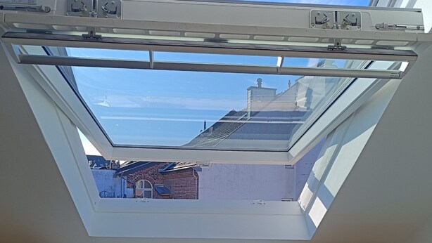 Een dakraam met uitzicht op een gebouw en een stoel.