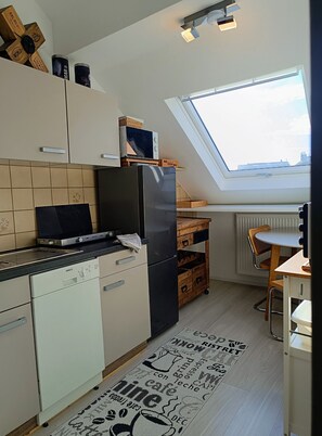A compact kitchen with a dishwasher, a black refrigerator, a microwave, and a small dining area with a table and chairs.