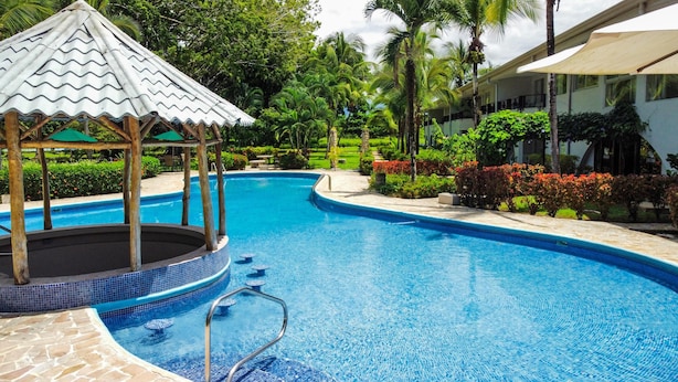 En swimmingpool med en pavillon, omgivet af frodig vegetation og palmer.