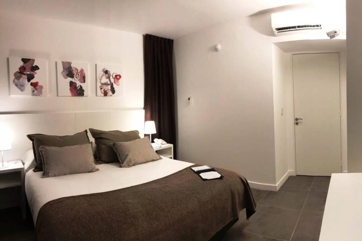 Ein Hotelzimmer mit Bett, Nachttischen, einem Fernseher, Wandbildern und einer Klimaanlage.
