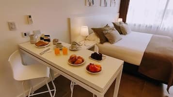 A hotel room with a bed, a bedside table with breakfast items, a chair, and a lamp.
