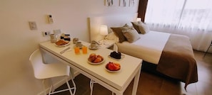 A hotel room with a bed, a bedside table with breakfast items, a chair, and a lamp. - RENTAL SUITES CAMPANA (Campana)