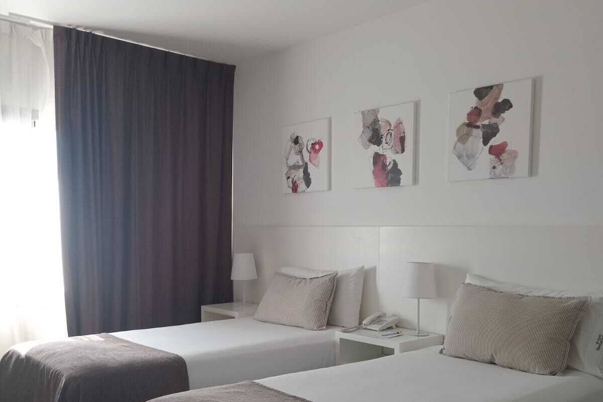 Ein Hotelzimmer mit zwei Betten, einem großen Fenster mit Vorhängen und abstrakter Kunst an der Wand.