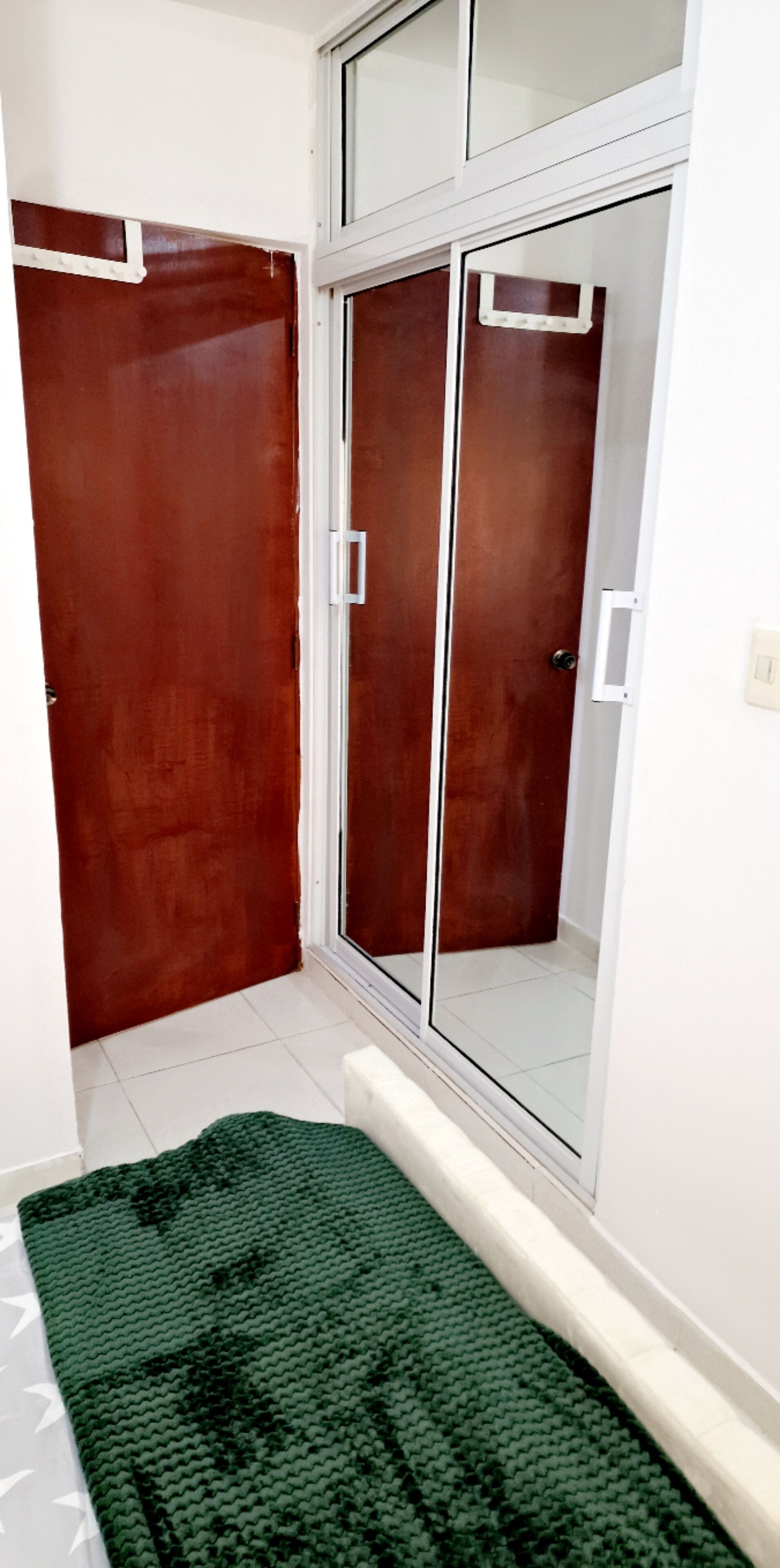 A room with a wooden wardrobe, a mirrored closet, and a green textured rug on the floor.