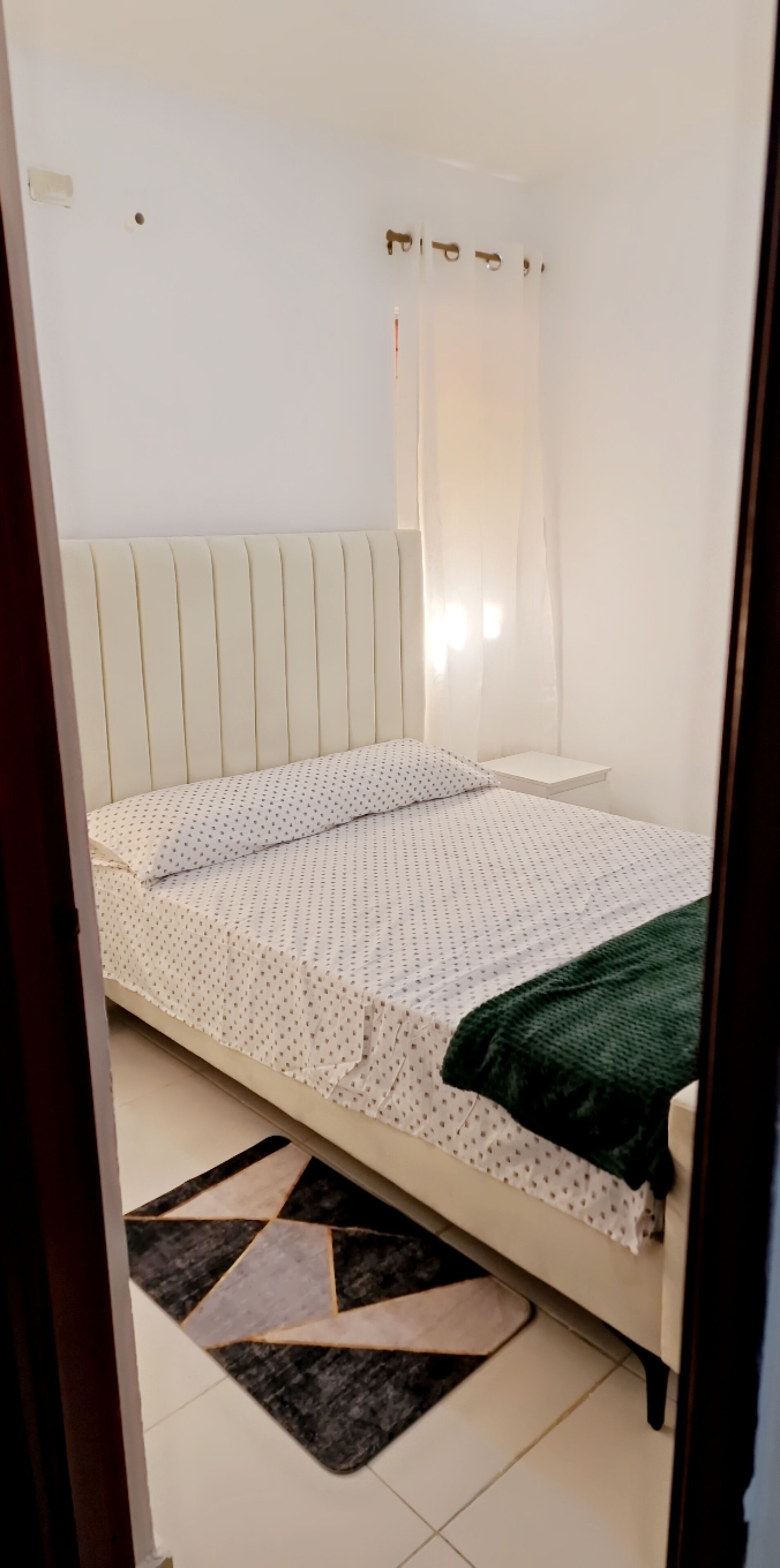 A bedroom with a bed, a bedside table, a nightstand, and a window with curtains.