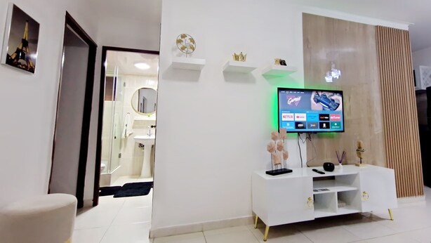 A modern living room with a flat-screen TV, white entertainment unit, and a black refrigerator. - Apto, Res, Carmen Renata Iii, a 8 Minutos de la Embajada Americana sto dgo (Pantoja)