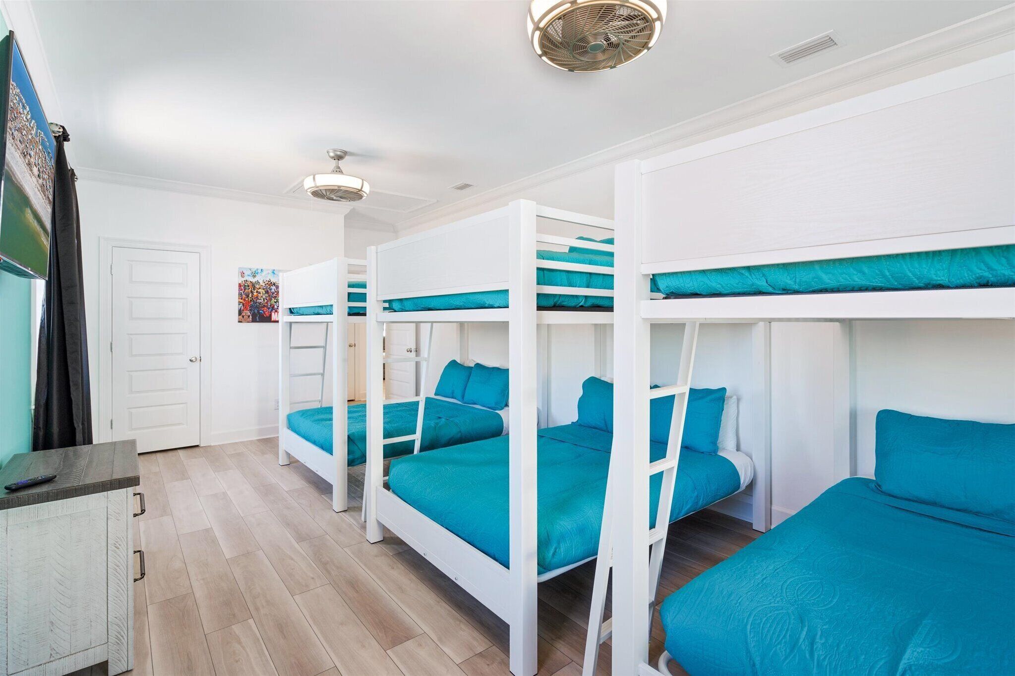 A room with bunk beds, a white door, a small cabinet, and a ceiling fan.