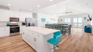 Un'ampia cucina con mobili bianchi, un'isola centrale e una zona pranzo con sedie color acquamarina.