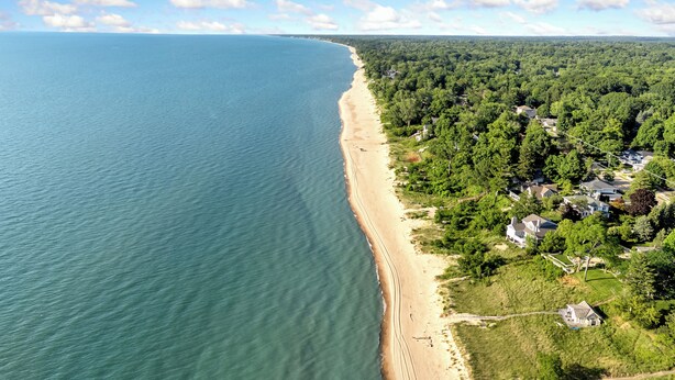 Vue aérienne d’une zone côtière comprenant une plage, une forêt dense et des habitations.