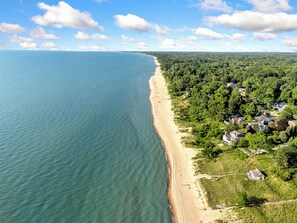 Luftaufnahme einer Küstenlandschaft mit Strand, dichtem Wald und Wohngebäuden.