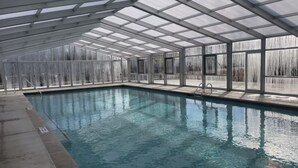 Une piscine intérieure dotée d’un toit en verre, d’une eau cristalline et d’un sol carrelé.