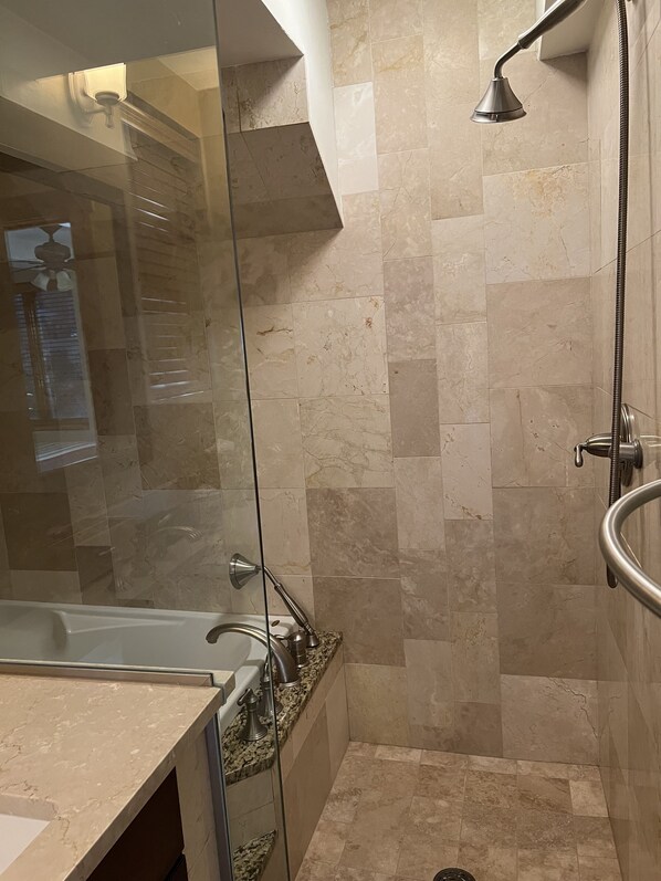 A modern bathroom with a glass shower enclosure, a bathtub, and a vanity with a marble countertop.