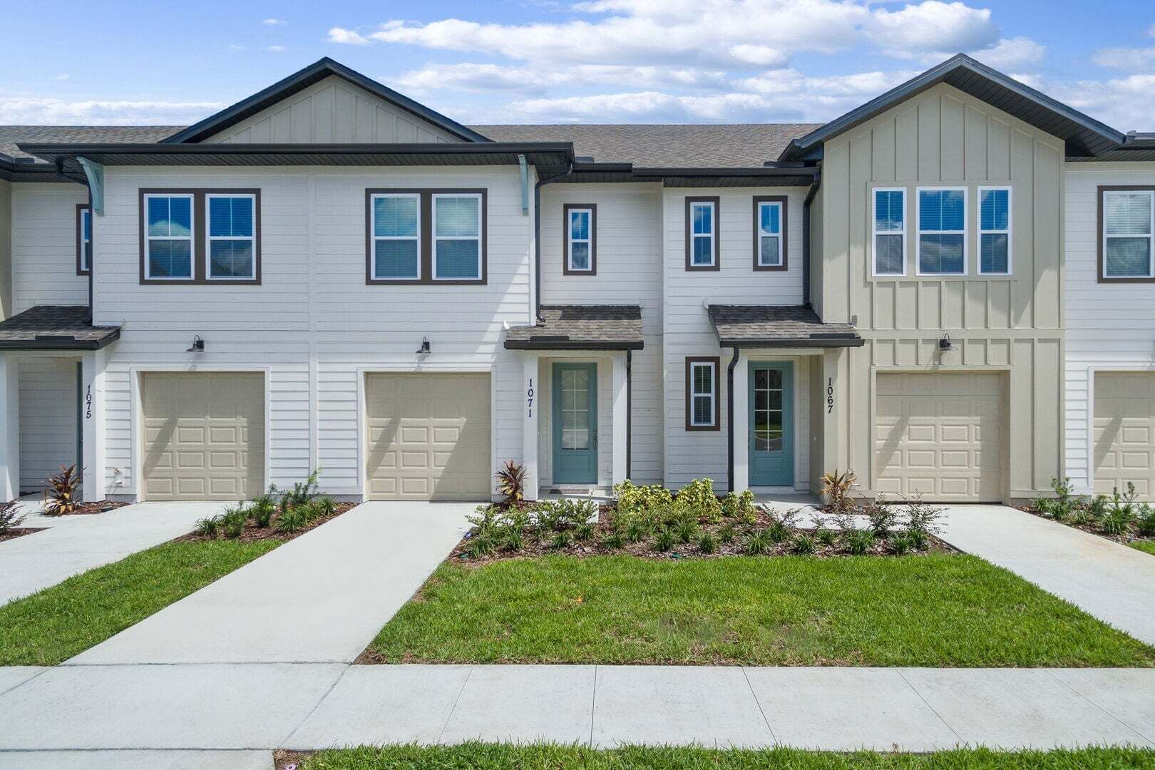 A two-story residential building with a front driveway, a green door, and a well-maintained lawn.
