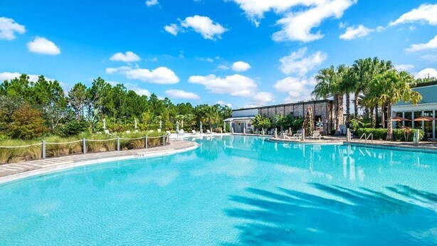A large outdoor swimming pool with a clear blue sky, surrounded by palm trees and a building with a covered area. - 3 BR, 2.5 BA Villa | Sleeps 8! (Davenport)