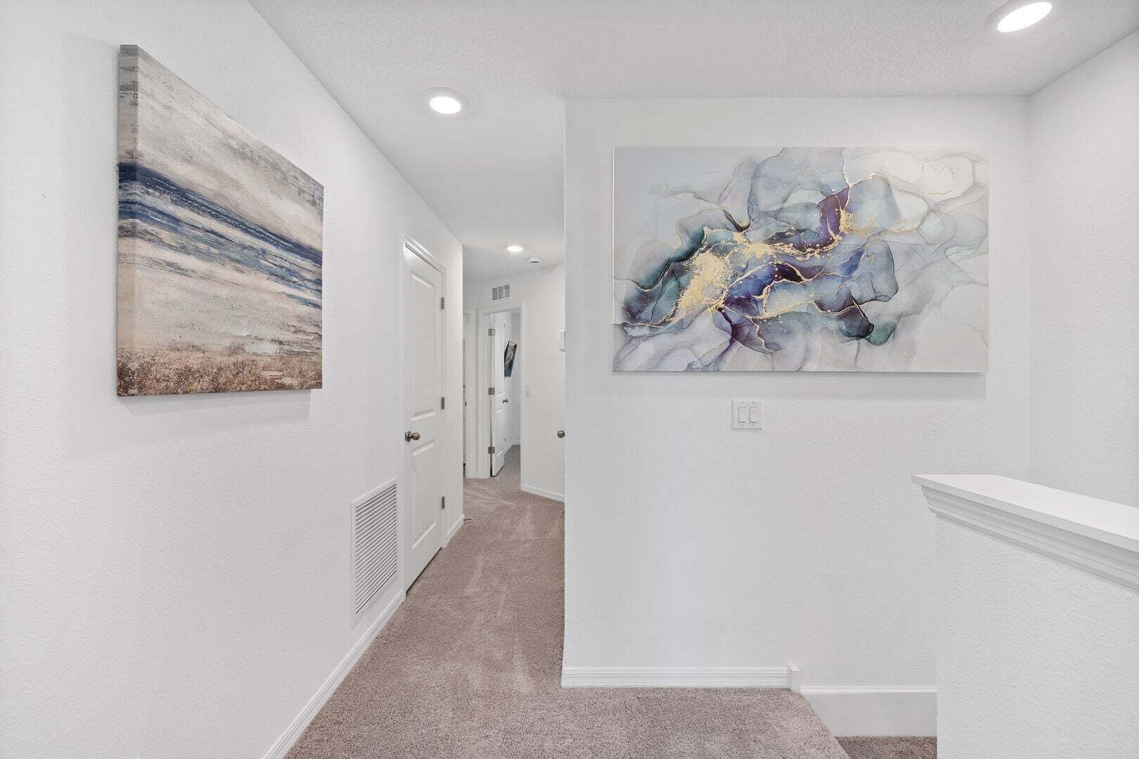 A hallway with white walls, a marble artwork, and a white fireplace.
